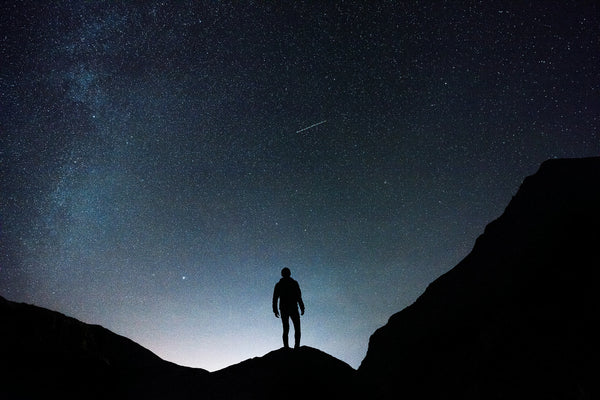 Silhouette of a person standing on a hill under a starry night sky, symbolizing the journey of finding relief and upliftment with Lockhold products after overcoming pain and challenges